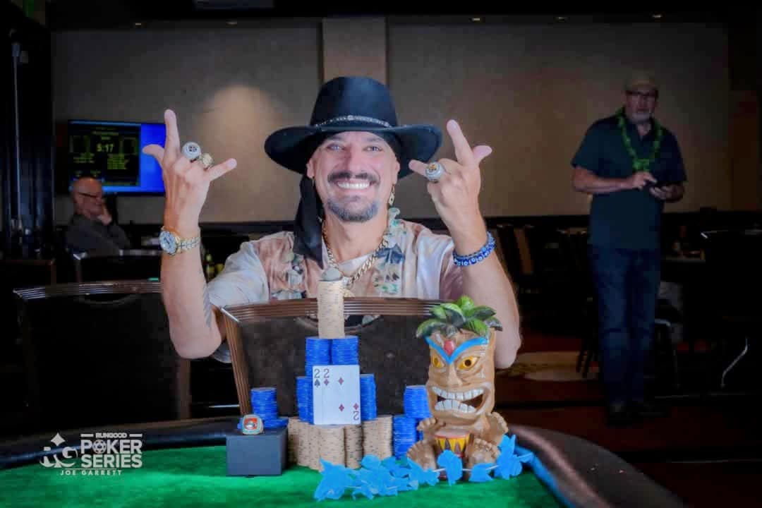 Joey holding up two championship rings behind a Run Good Poker Series trophy and chip stacks